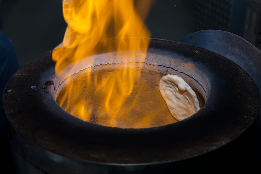 white plain raw naan bread in Tandoor oven with fire flame.